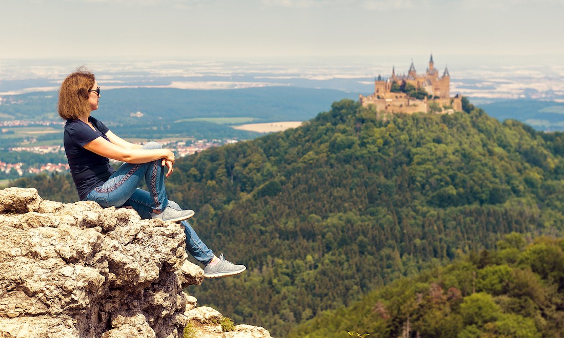 Tourist sitting on cliff looking at castle in background