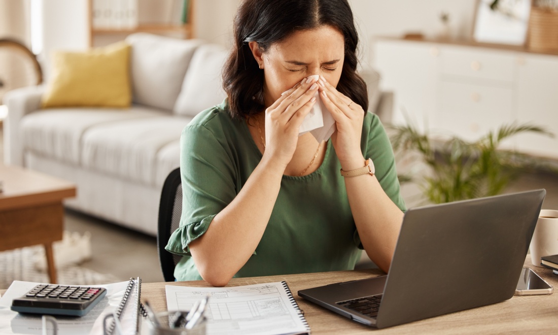 Sick woman sneezing into tissue behind laptop. Kerstin Brunner: 4 steps to keep your business running when you are absent  