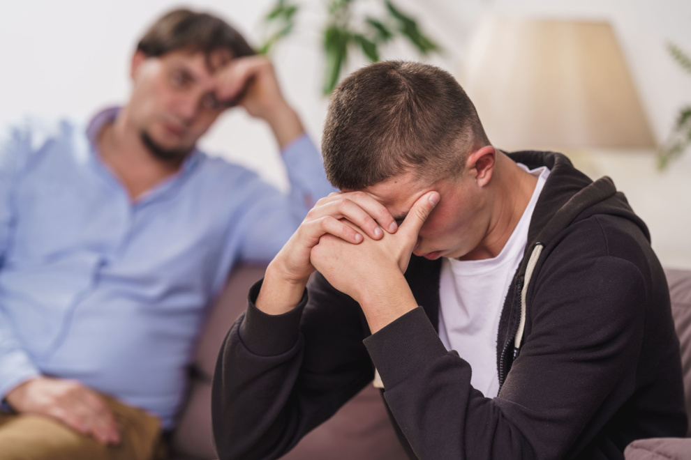 sad teenager with head in hands next to father