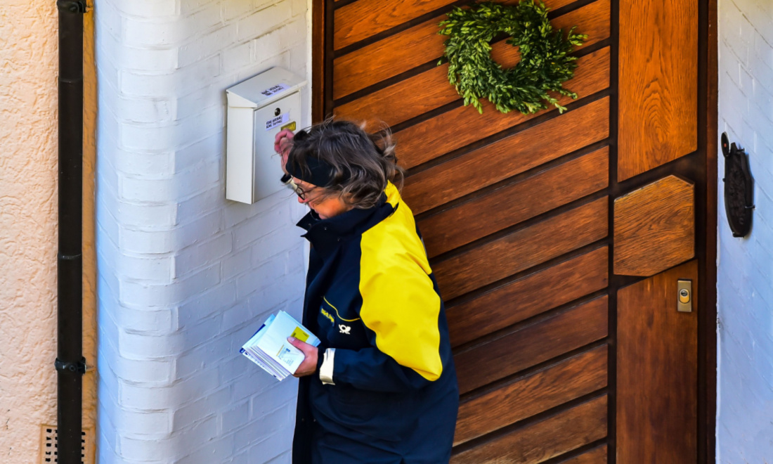 Postal worker in yellow jacket delivering letters to a house with a brown door and wreath